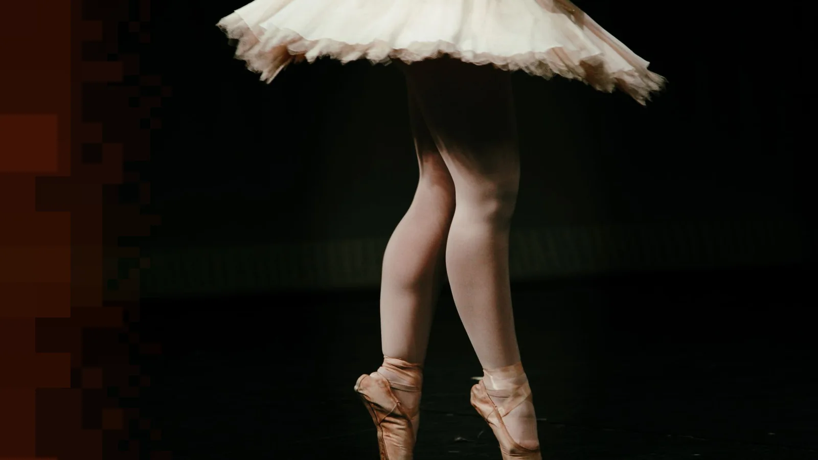 Bena til en ballettdanser på tåspiss i rosa ballettsko, med et hvitt tyllskjørt som virvler rundt på en mørk scene