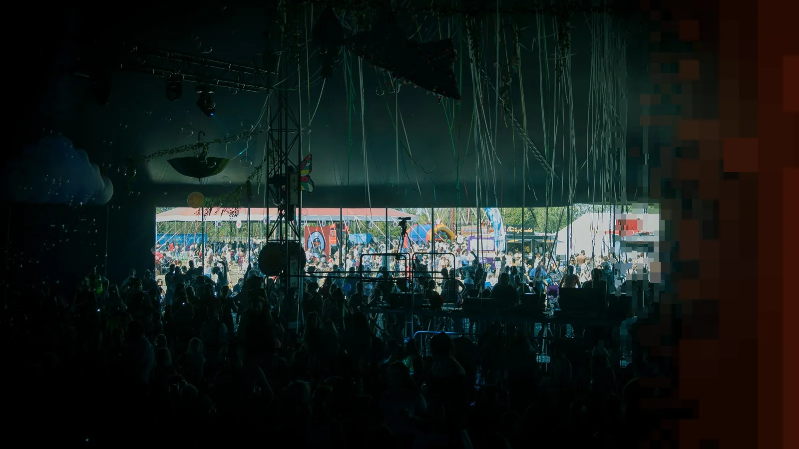 Publikum i silhuett i et mørkt festivaltelt, med en solfylt festivalplass synlig gjennom åpningen bak scenen