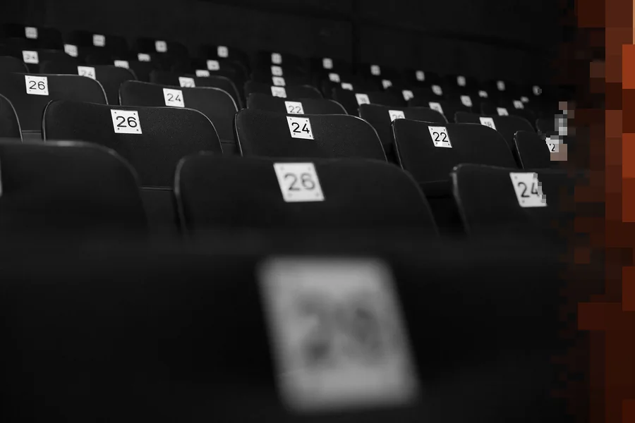 Rader av svarte teaterseter med hvite nummerskilt, i svart-hvitt