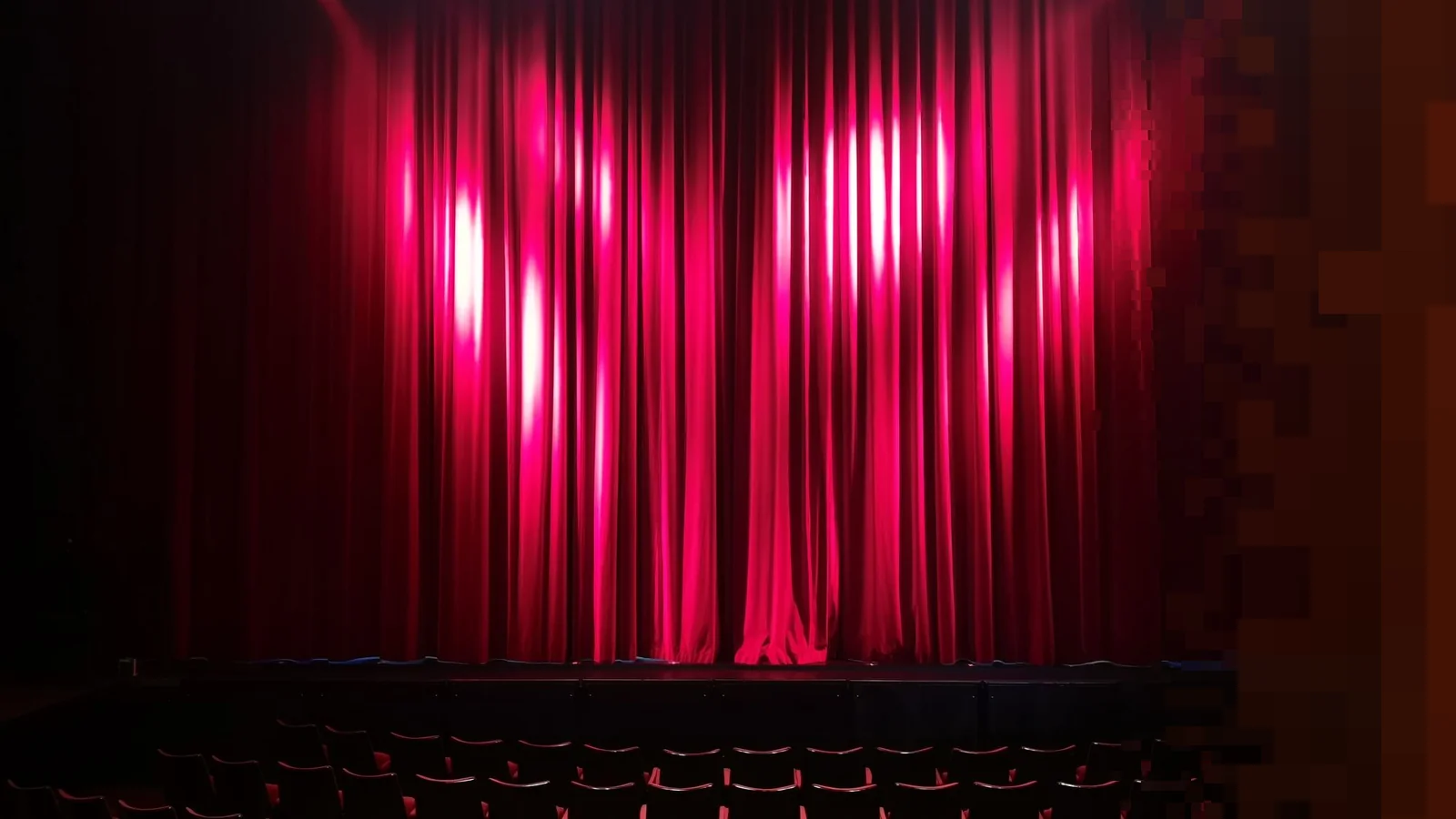 Tom teatersal med rød scenegardin og rader av seter foran scenen
