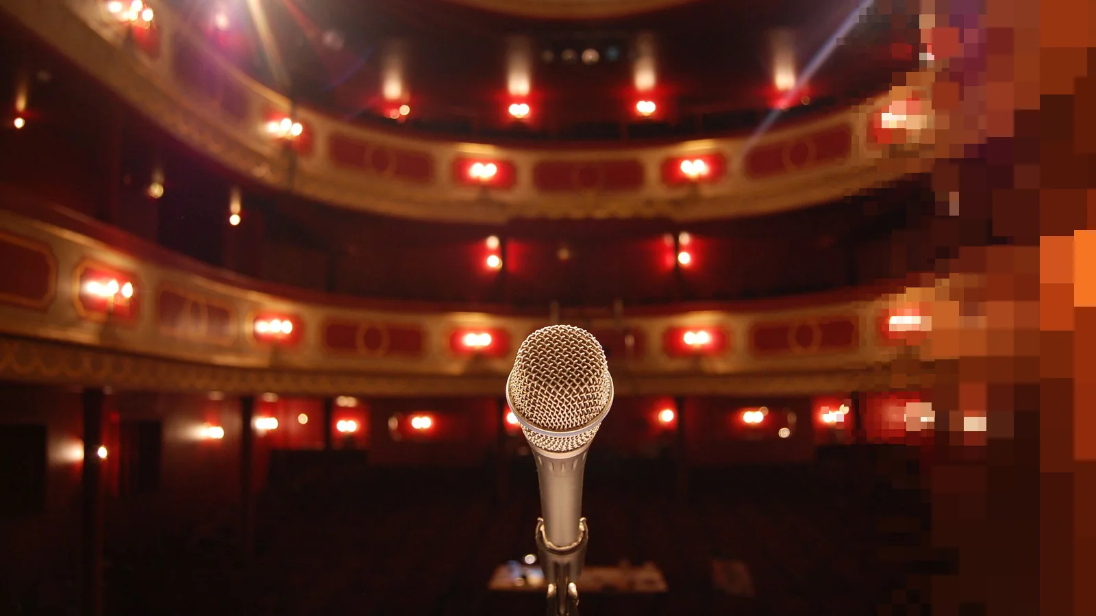En mikrofon på en scene med utsikt mot en ornamentert teatersal med balkonger og varme lys