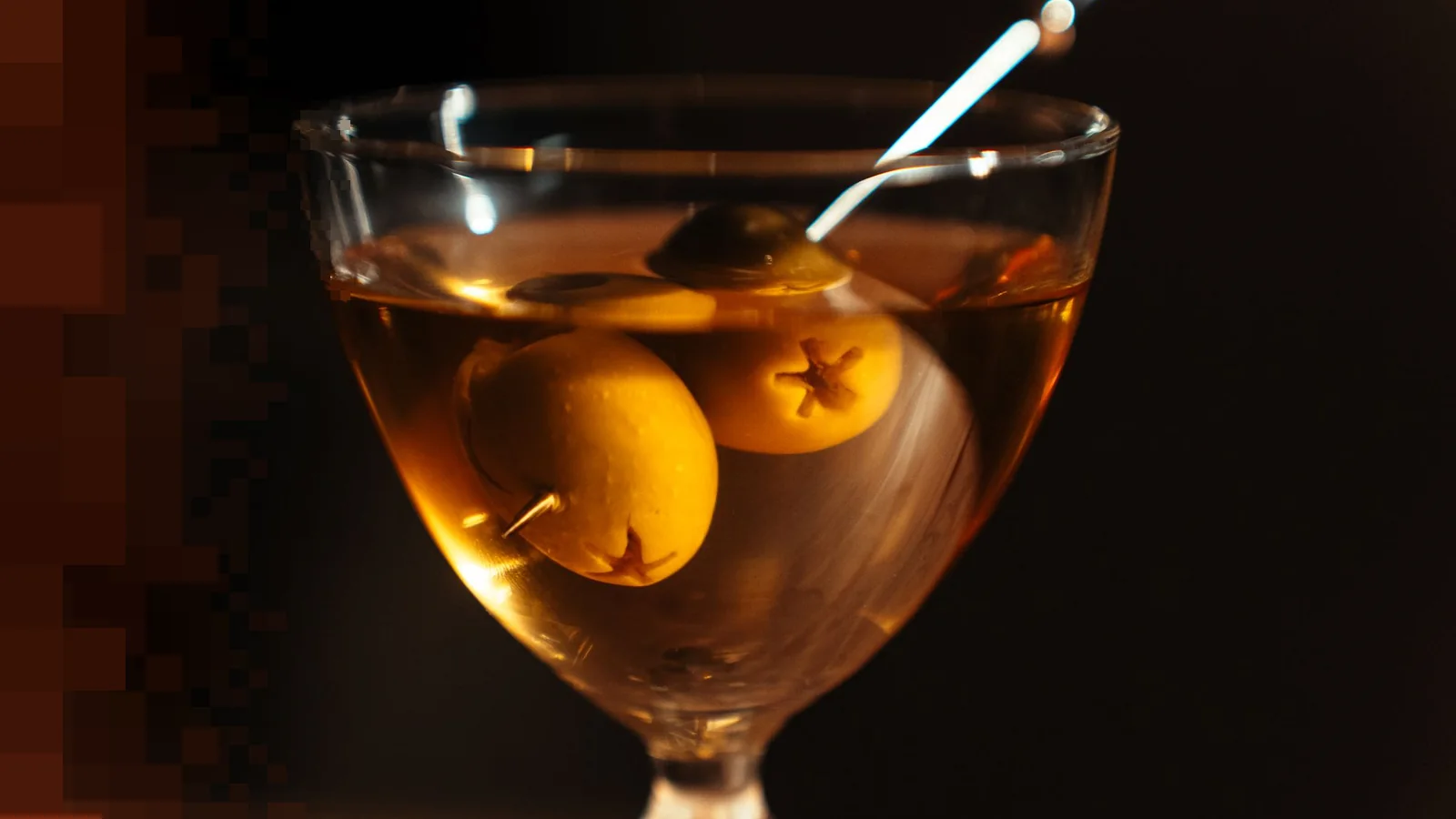 En dry martini med to grønne oliven på et cocktailspyd, i et stettglass mot en mørk bakgrunn