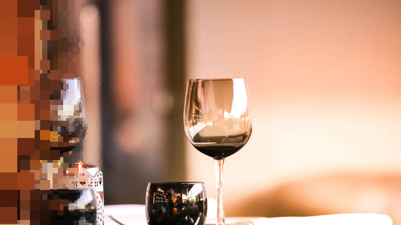 To vinglass med rødvin og et lite telys på et restaurantbord i varmt lys