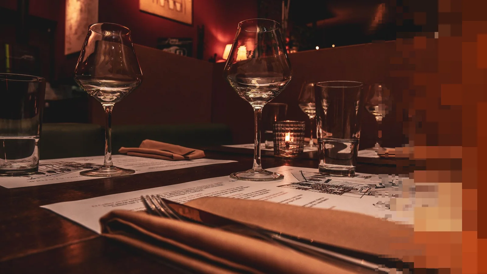Dekket bord med vinglass, servietter og levende lys på en restaurant i dempet lys