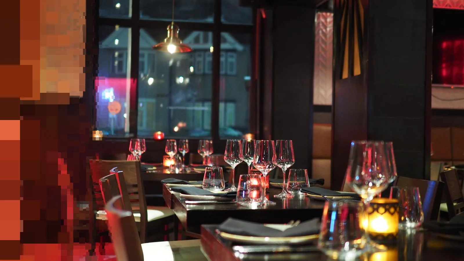 Restaurant om kvelden med dekkede bord, tomme vinglass og telys foran store vinduer