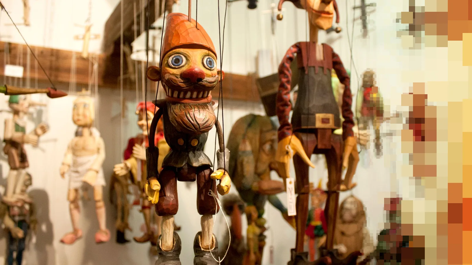 Håndlagde marionetter i tre henger i snorer på rekke, med en skjeggete dukke og en narr i rødt og brunt fremst