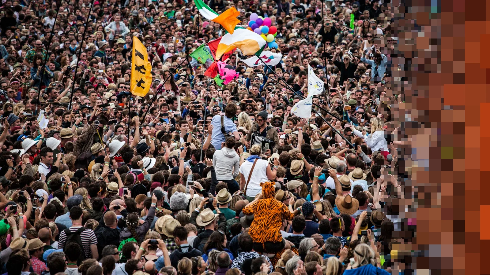 Et tett festivalpublikum med flagg og ballonger over hodene foran en scene
