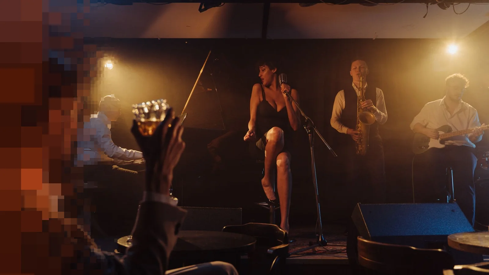 En jazzkvartett med sangerinne og saksofonist spiller under varme lamper på en liten klubbscene