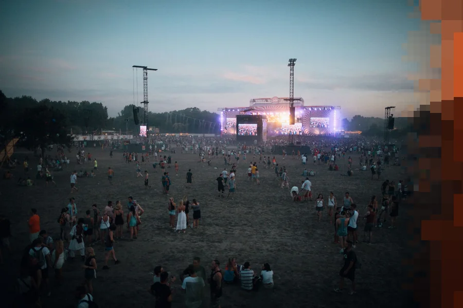 Festivalpublikum spredt utover en stor slette i skumringen med en opplyst scene langt bak