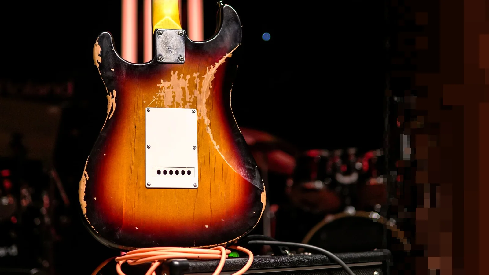 Slitt elektrisk gitar som lener seg mot en forsterker på en mørk scene