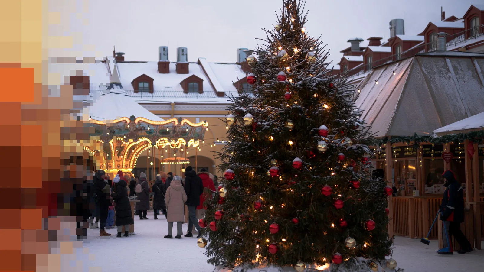 Stort pyntet juletre med lyslenker og en karusell på et snødekt julemarked