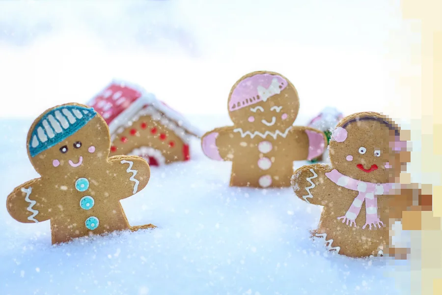 Tre pepperkakefigurer i snø med små pepperkakehus i bakgrunnen