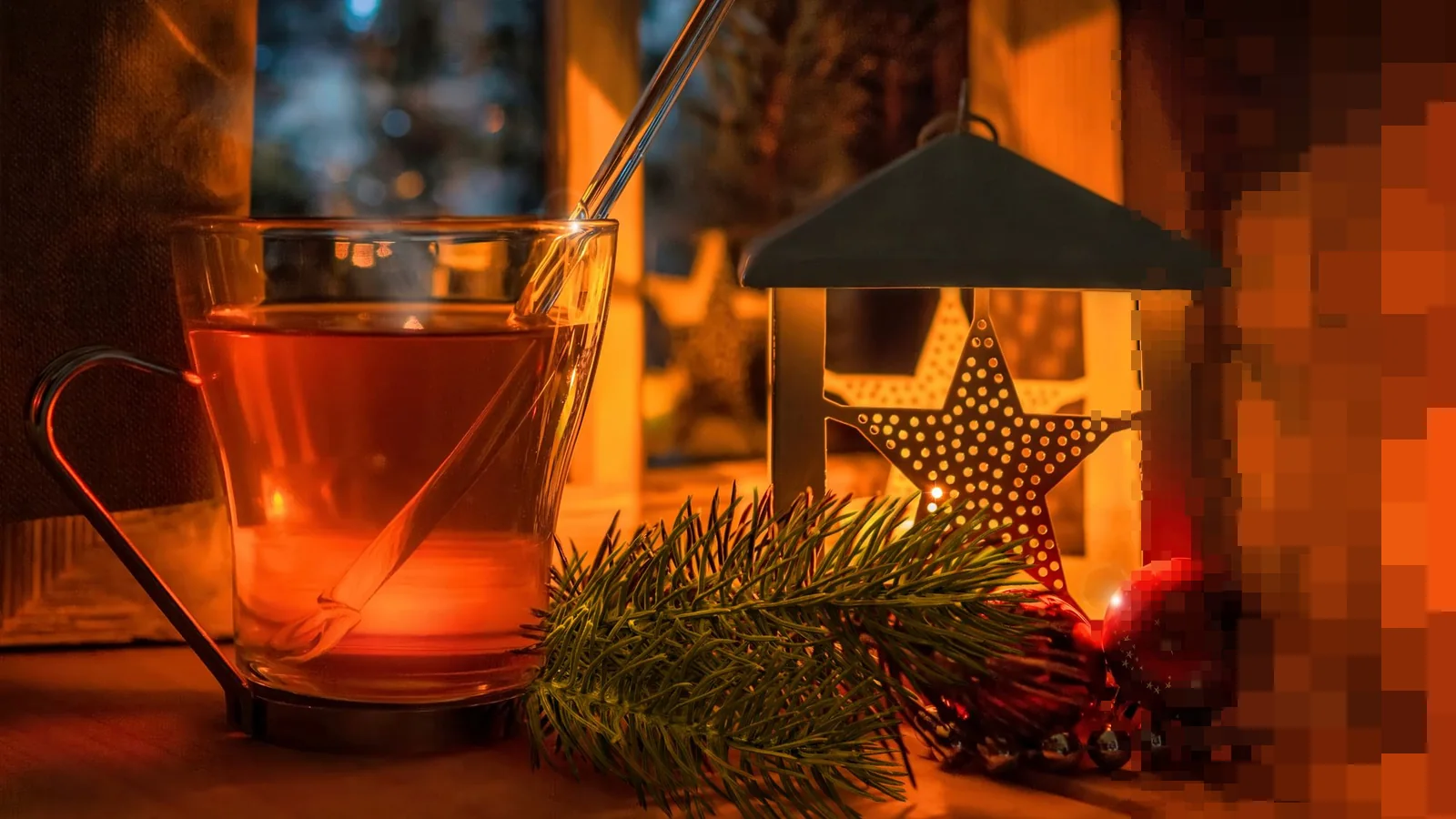 Et glass te og en julelykt med en stjerne i varmt lys, ved siden av grankvister