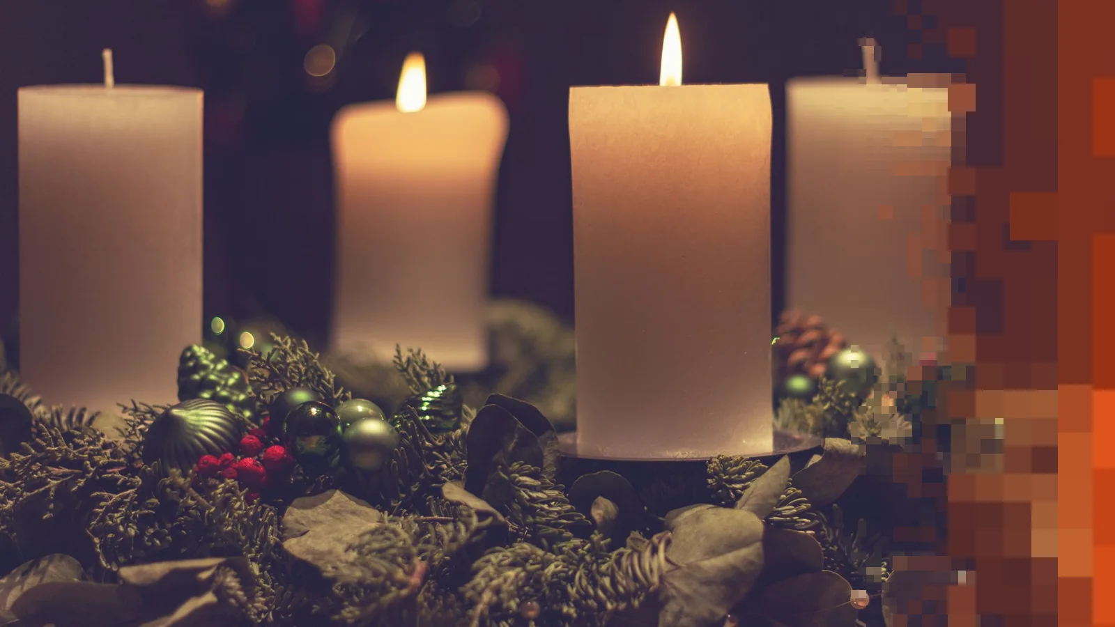 Fire hvite stearinlys, ett tent, i en adventskrans av gran og julepynt mot mørk bakgrunn
