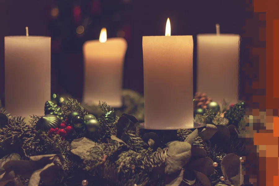 Fire hvite stearinlys, ett tent, i en adventskrans av gran og julepynt mot mørk bakgrunn
