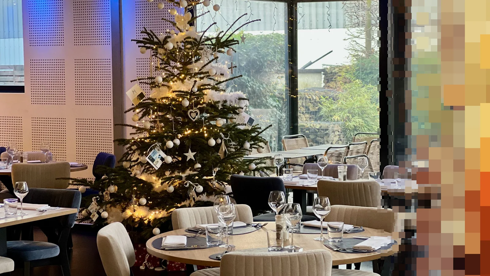 Restaurantsal med dekkede bord og et pyntet juletre ved et stort vindu