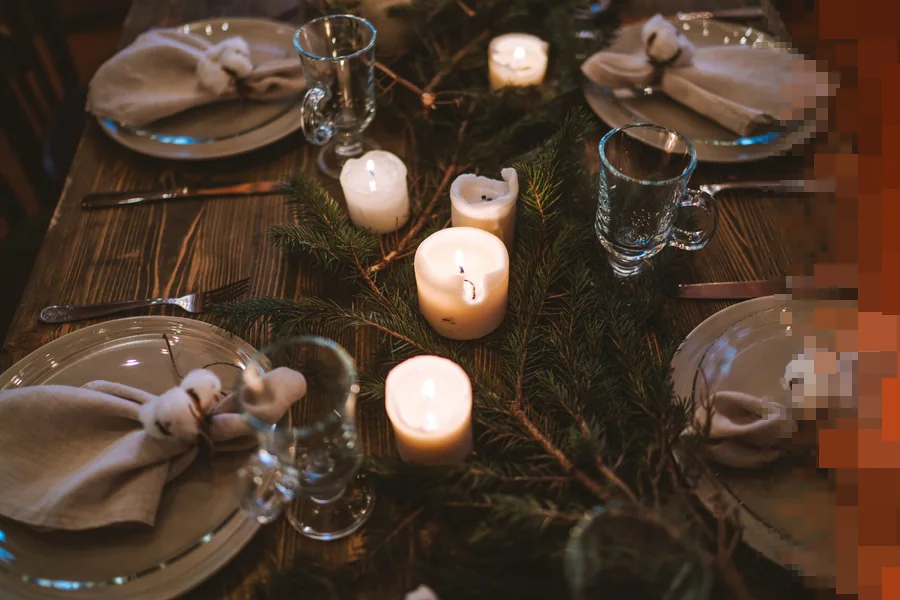 Dekket julebord med hvite tallerkener, stearinlys og grankvister på et mørkt trebord