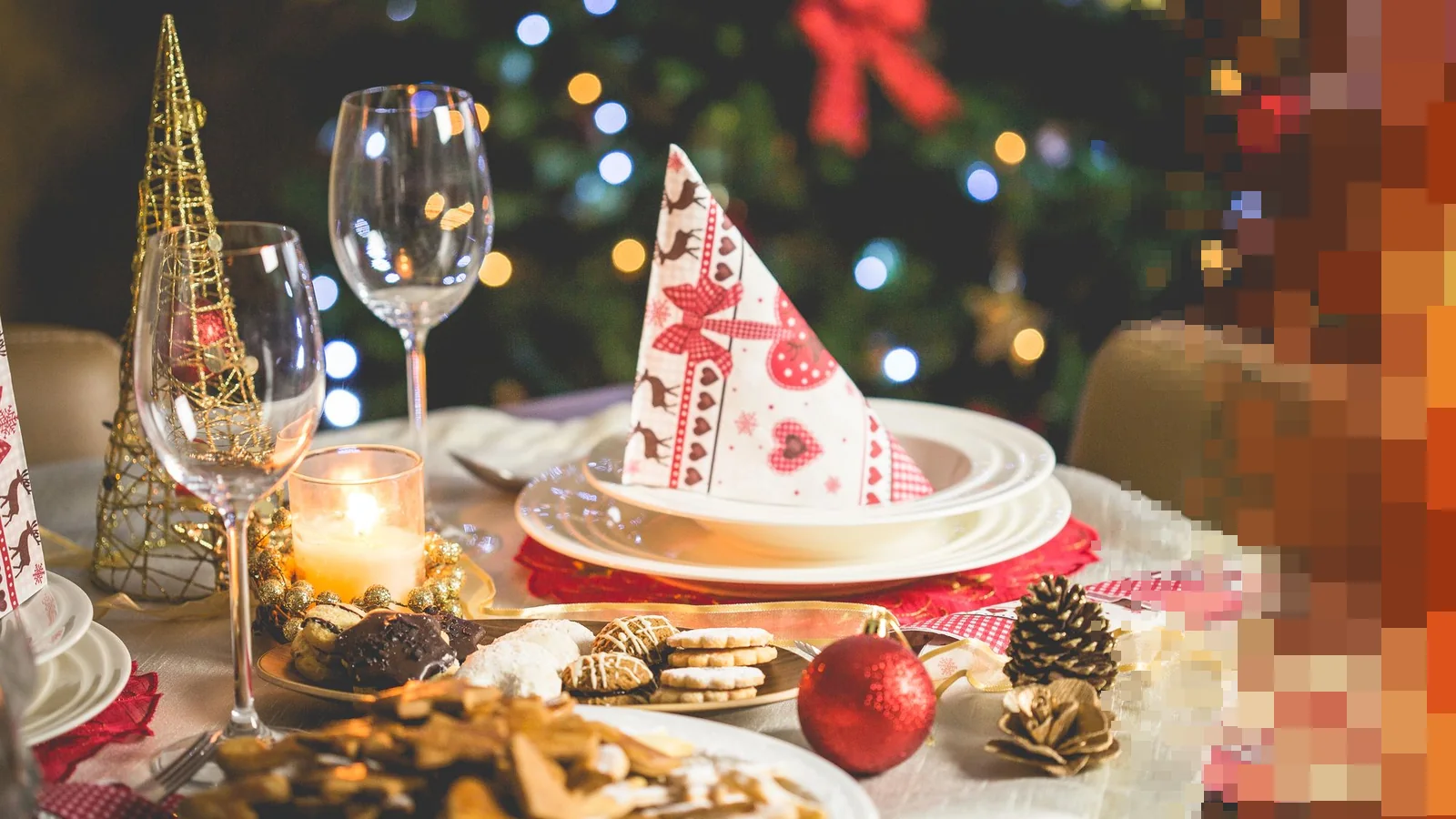 Et pyntet julebord med vinglass, levende lys, julekuler og pepperkaker