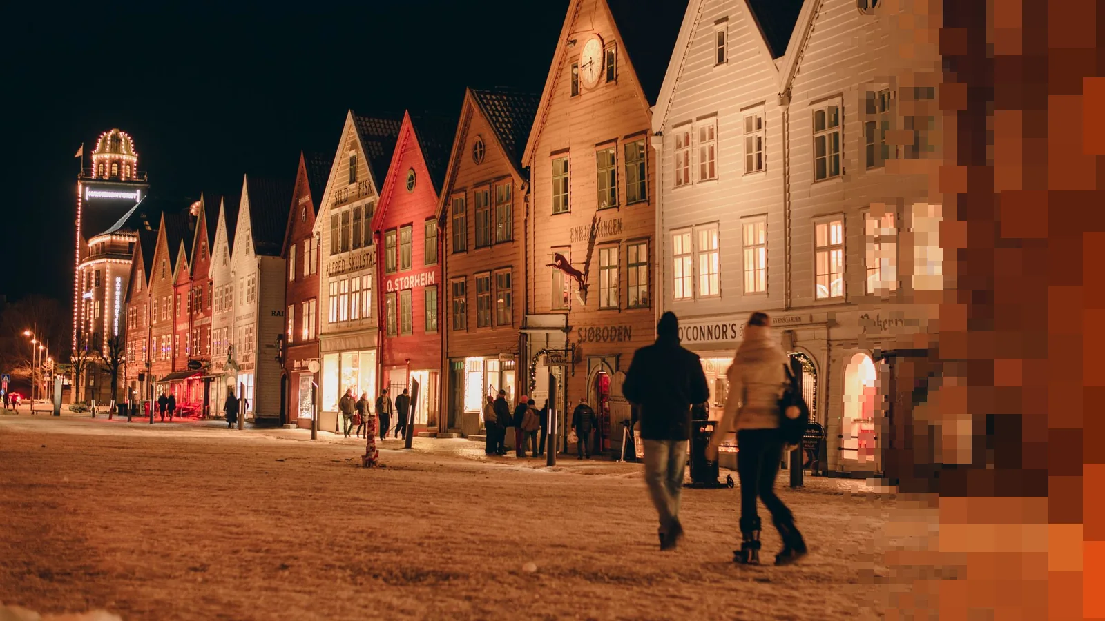 Bryggen i Bergen en vinterkveld, med opplyste trehus og folk på vei gjennom snøen