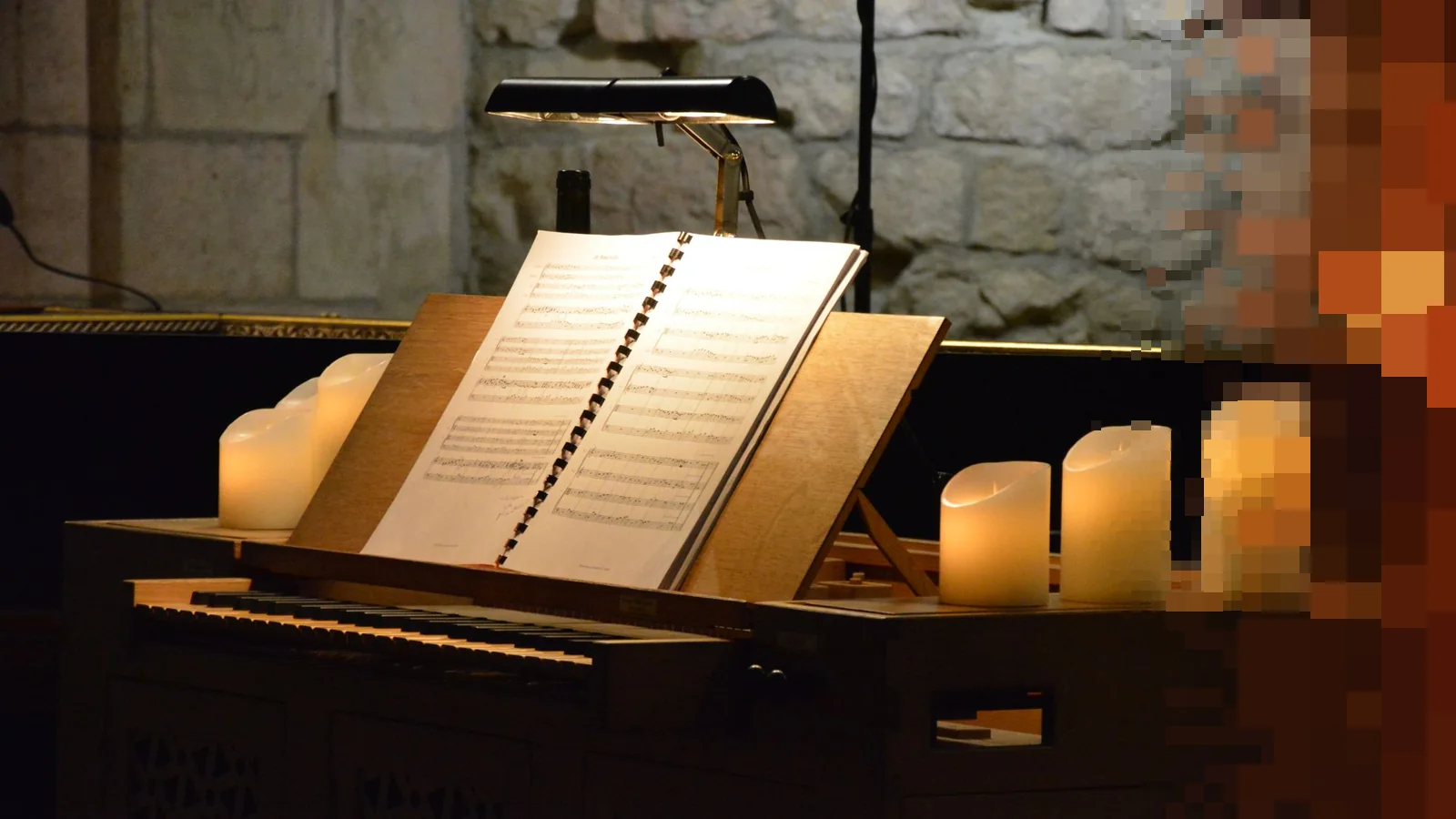 Noteark på et lite orgel mellom stearinlys i et kirkerom med steinvegger