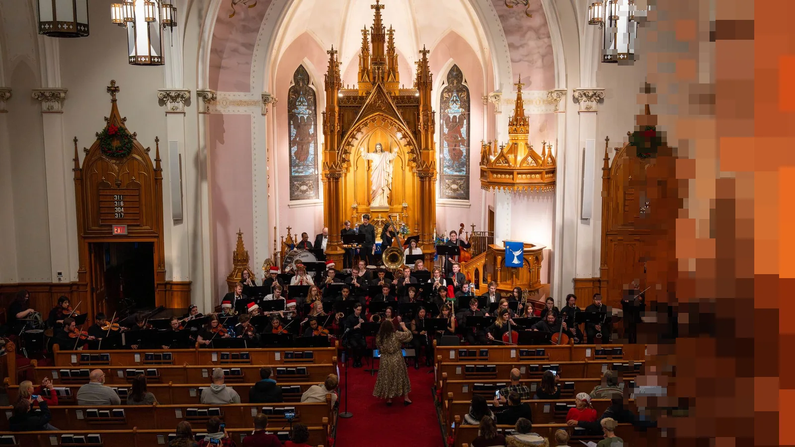 Et orkester spiller julekonsert foran et forgylt alter i en kirke med fullsatte benker