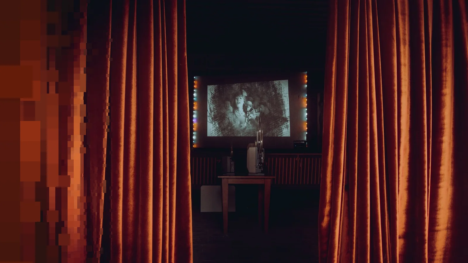 Et lite visningsrom med tunge rustrøde fløyelsgardiner og et svart-hvitt filmbilde på lerretet bak en projektor