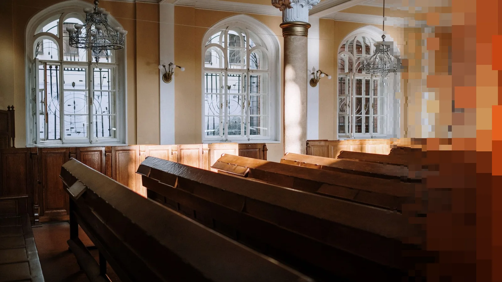 Solfylt kirkerom med trebenker og lysekroner under buede vinduer