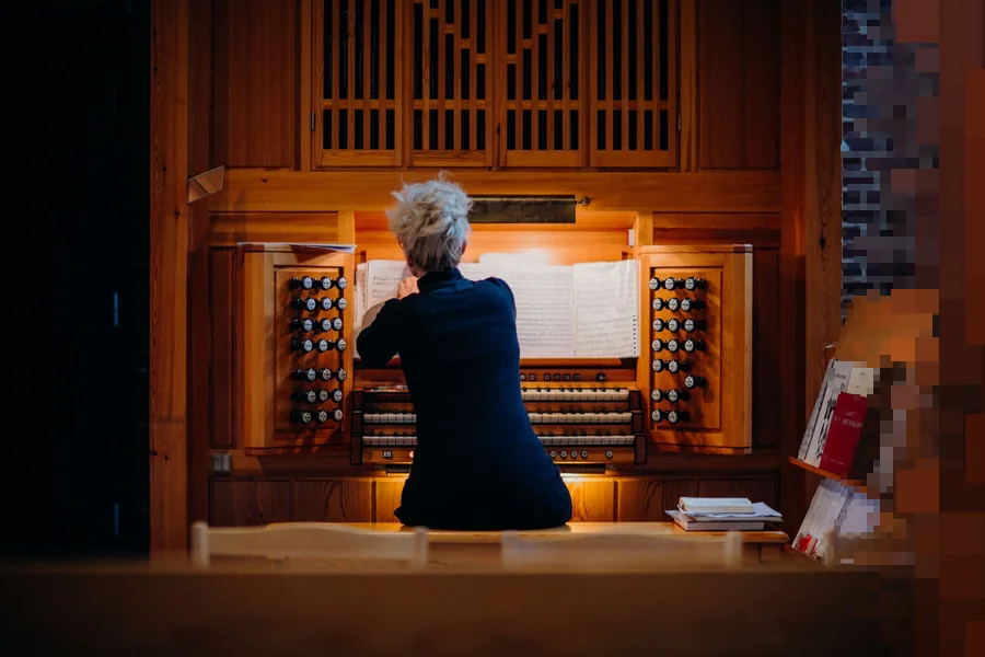 Organist sett bakfra ved et orgel av tre med oppslåtte noter i et kirkerom med mursteinsvegg