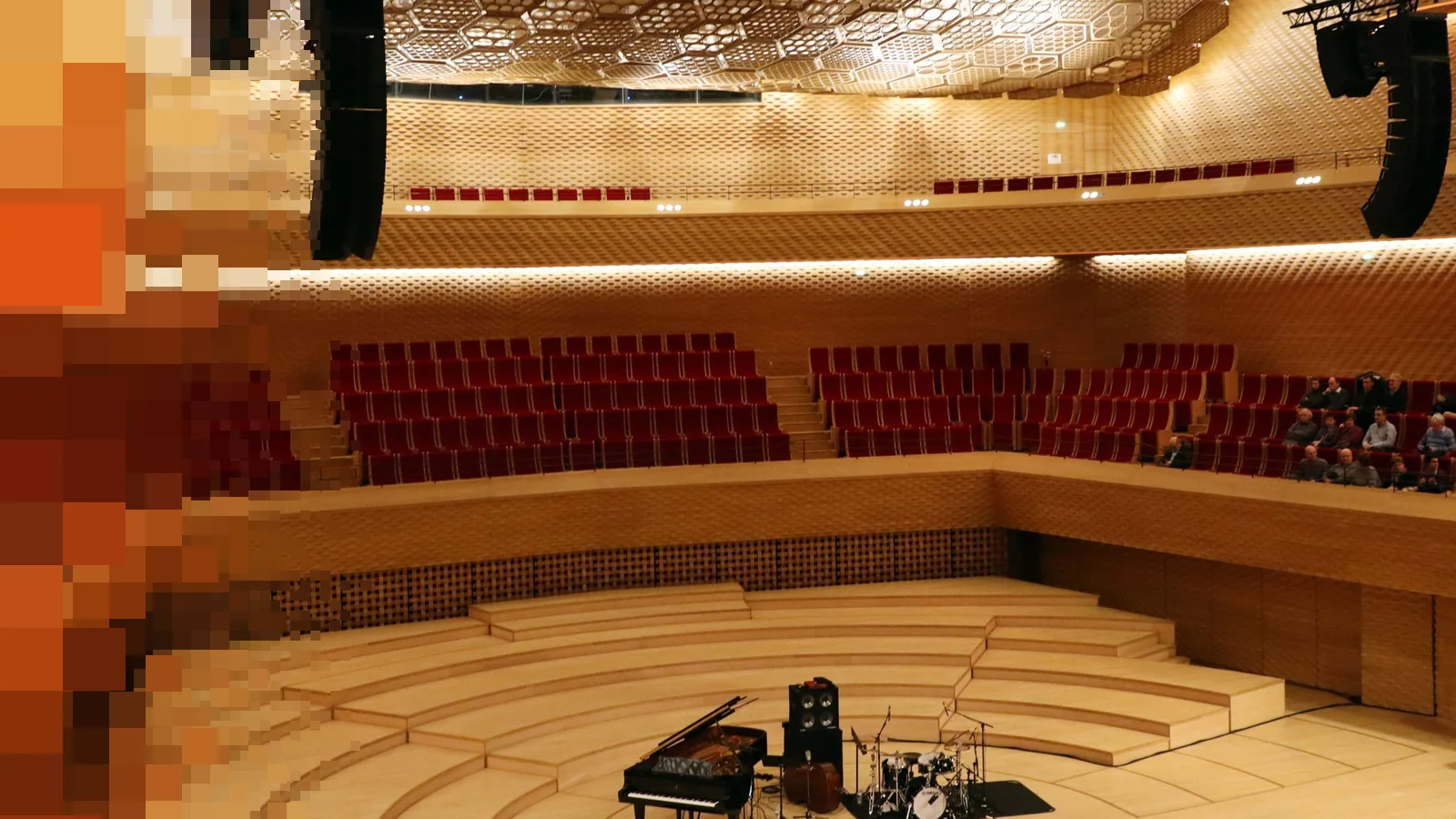 En tom konsertsal med røde seter på to balkonger og et flygel og et trommesett på en lys tregulvscene