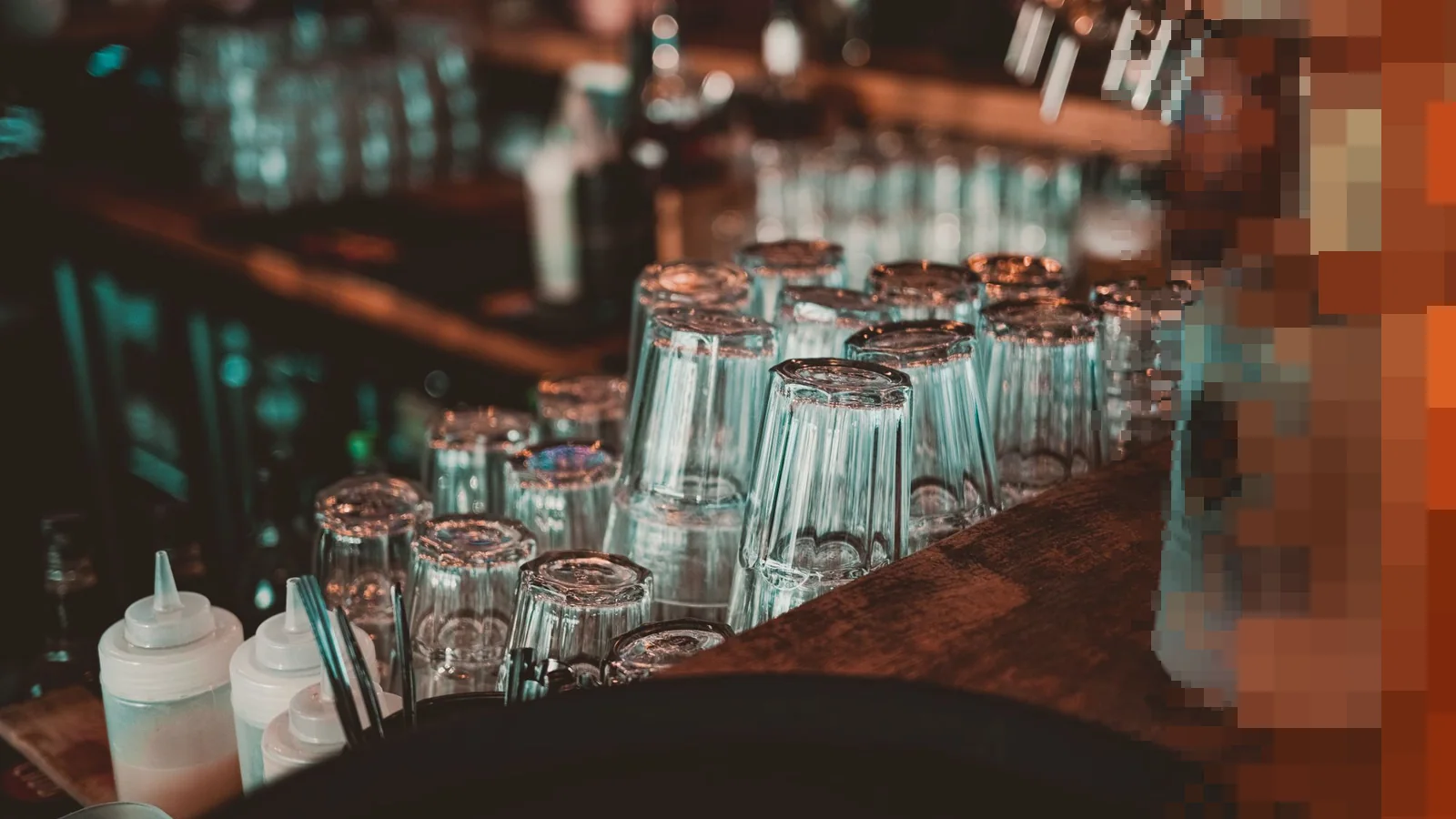 Mørk bardisk med omvendte glass på rekke og tappekraner i bakgrunnen