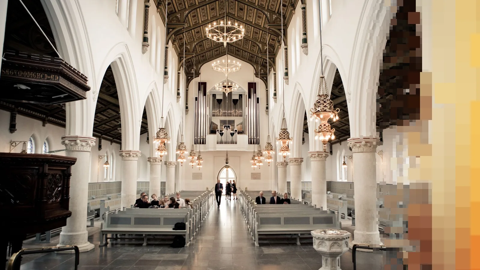 Langskipet i en lys kirke med hvite buer, trebenker og en orgelfasade i enden