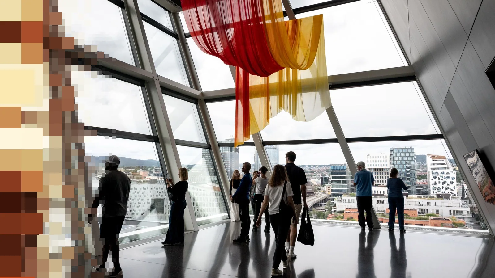 Besøkende ved høye glassvinduer med utsikt over byen i et moderne museumsbygg