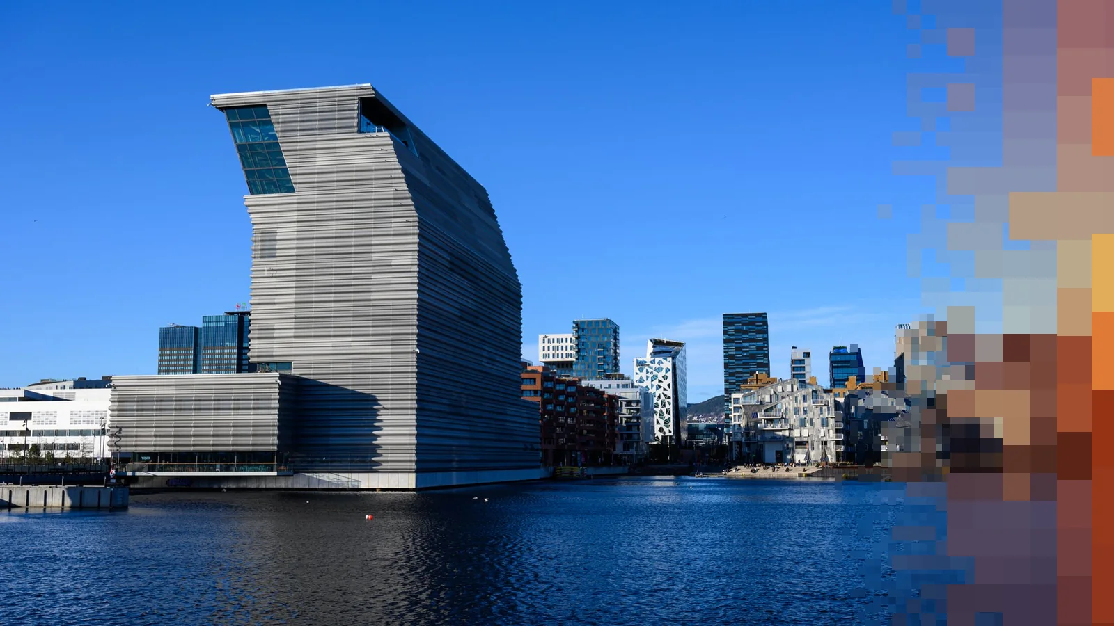 MUNCH-bygget i Bjørvika i Oslo står høyt over fjorden en solrik dag, med byen bak