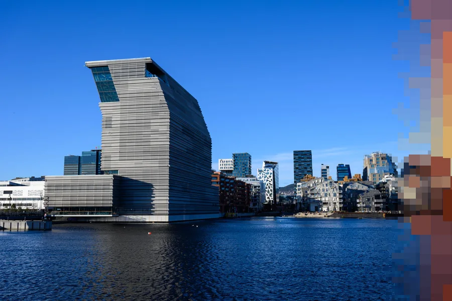 MUNCH-bygget i Bjørvika i Oslo står høyt over fjorden en solrik dag, med byen bak