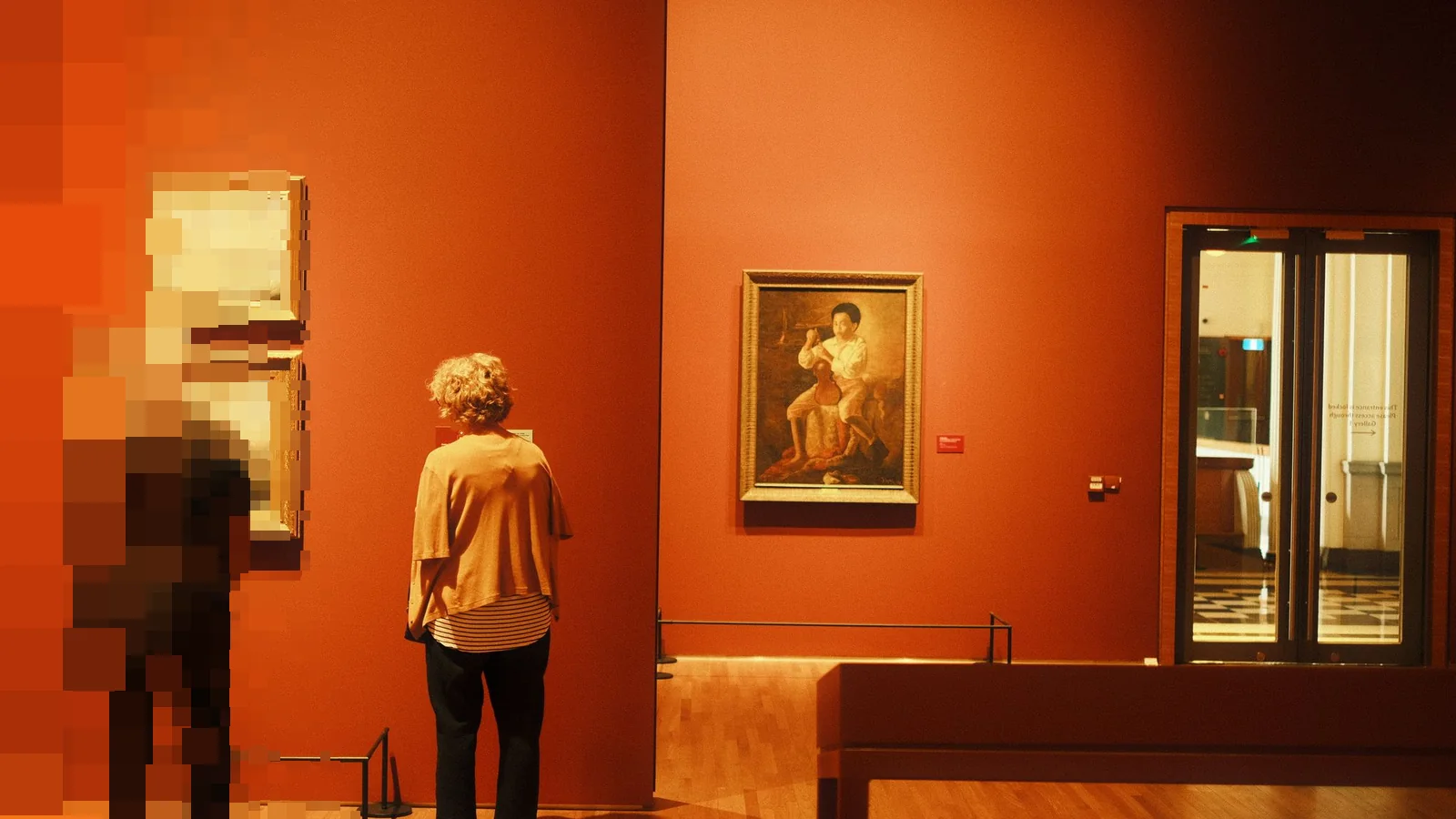 To besøkende ser på malerier på en rød vegg i et kunstmuseum