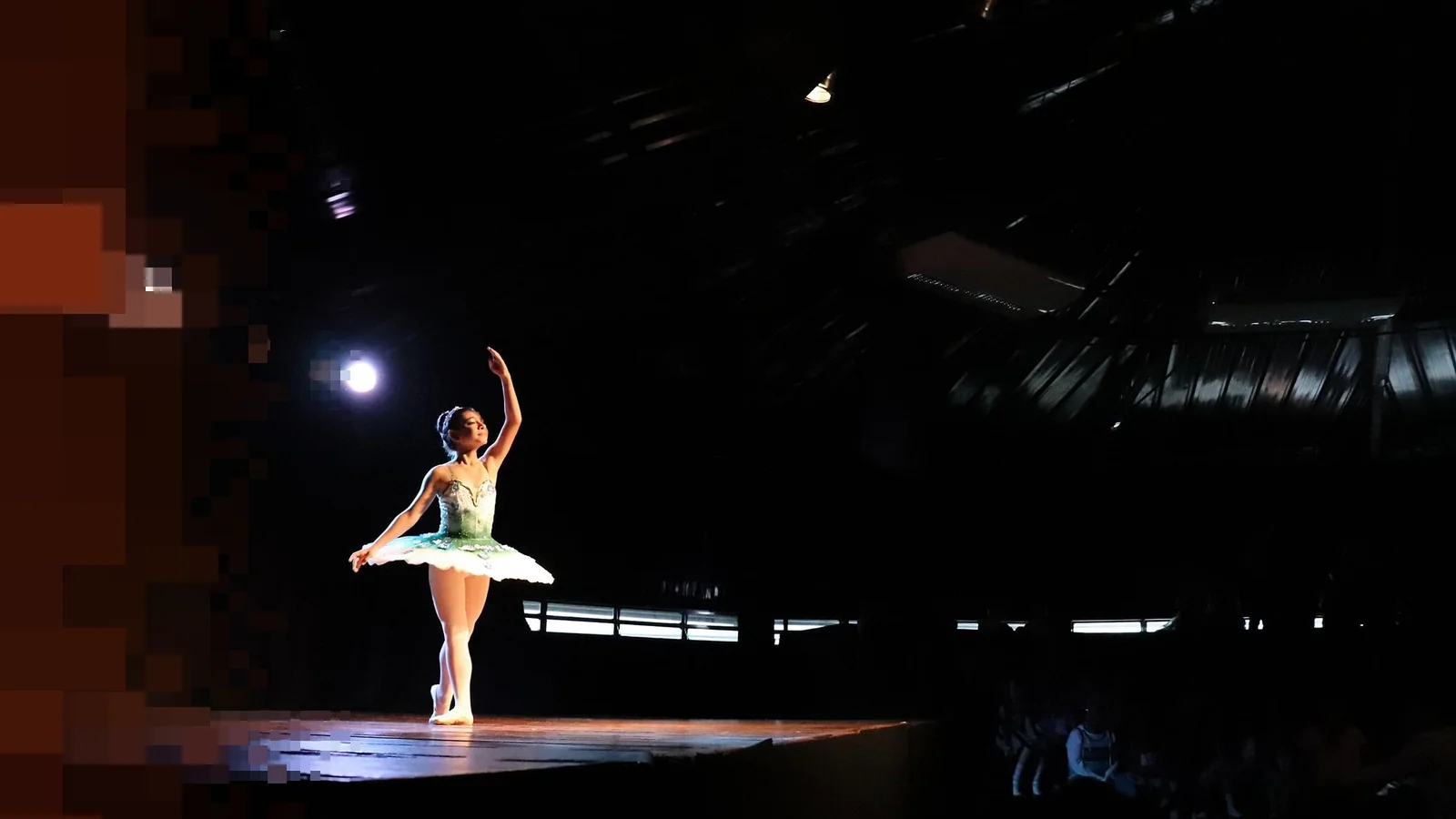 En ballerina i grønn tutu danser alene på en mørk scene med ett lyskaster