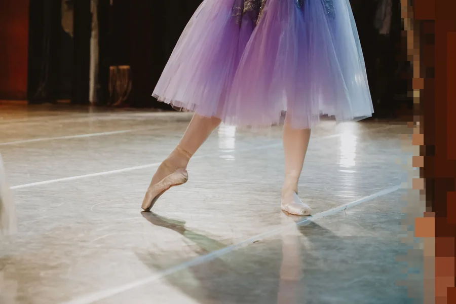 Ben og spisse ballettsko under en lilla tutu på et lyst scenegulv