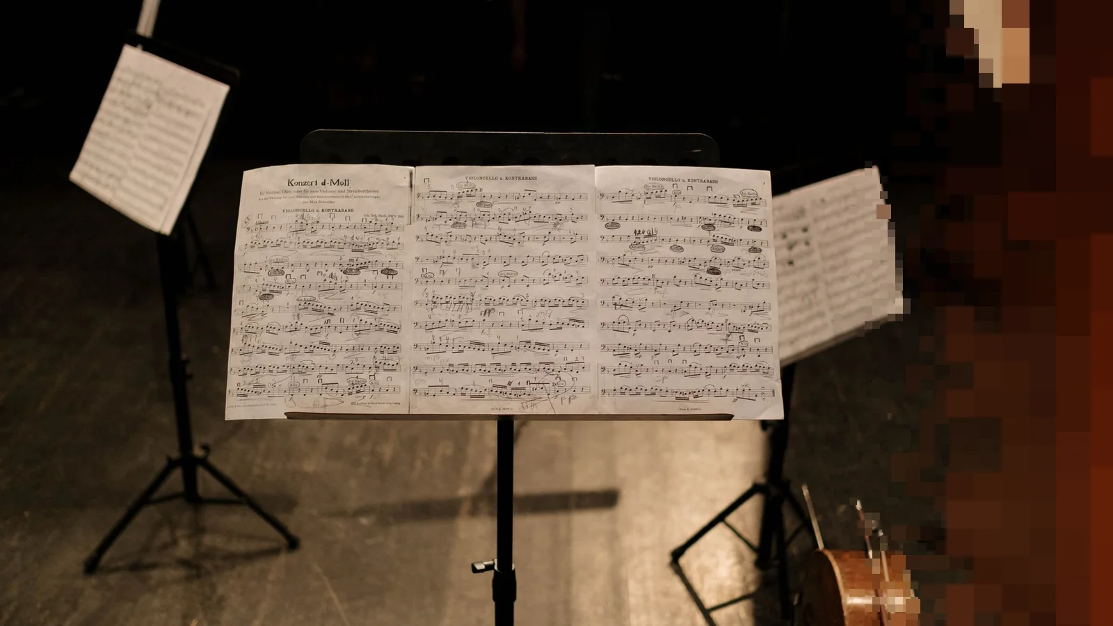 Et notestativ med oppslått partitur foran tomme stoler og en kontrabass på en mørk konsertscene