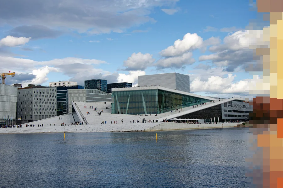 Operaen i Oslo sett fra vannet en dag med skyer, med folk som går på det skrå marmortaket