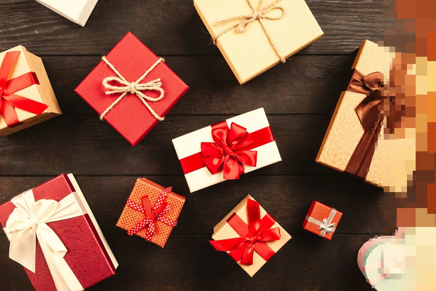 Innpakkede gaver med sløyfer i rødt, hvitt og brunt, sett ovenfra på et mørkt trebord