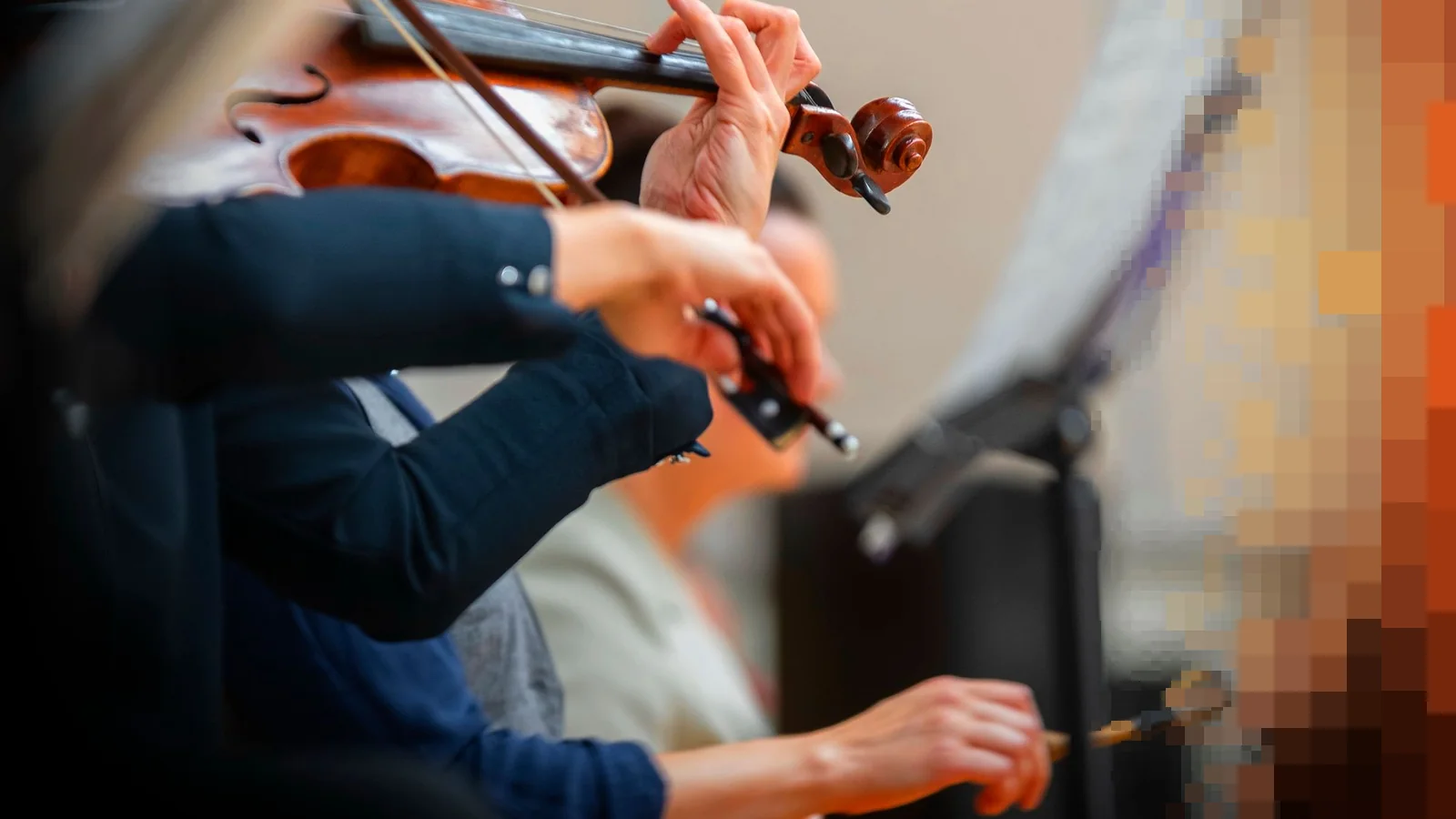 Nærbilde av hender som holder fioliner og buer i et orkester, med noter i bakgrunnen