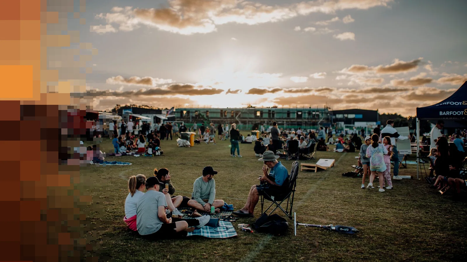 Festivalpublikum sitter på pledd og stoler i gresset i solnedgang med telt og boder i bakgrunnen