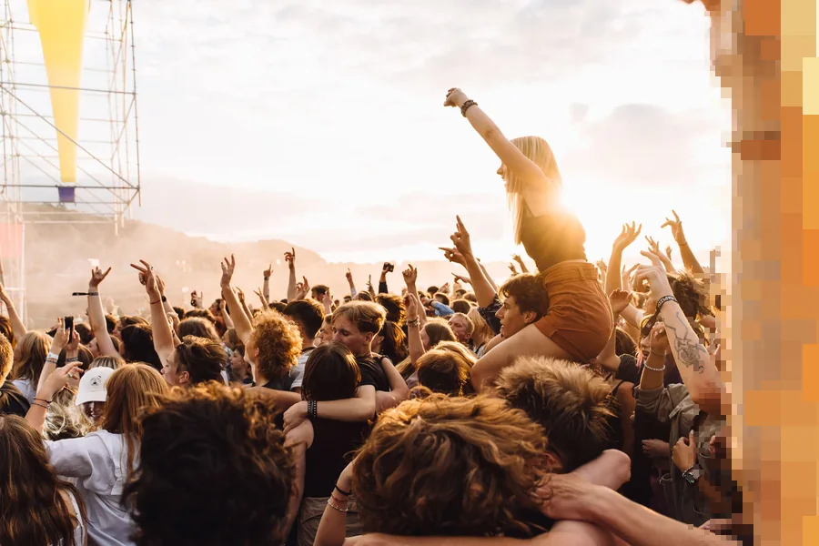 Festivalpublikum med armene i været foran en scene i motlys fra kveldssolen