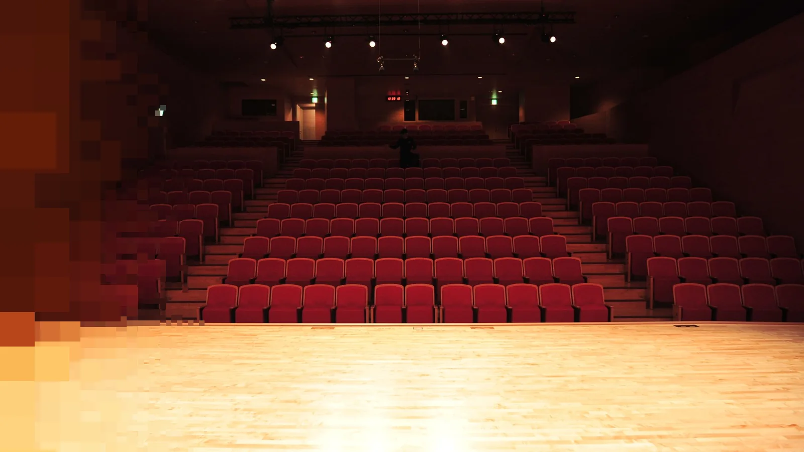 Tomt auditorium med røde seter i rader og et lyst scenegulv foran