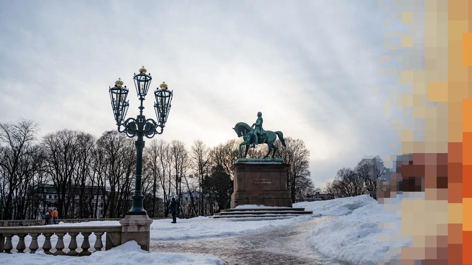 Snødekt park i Oslo med rytterstatue og en pyntet gatelykt mot en overskyet vinterhimmel