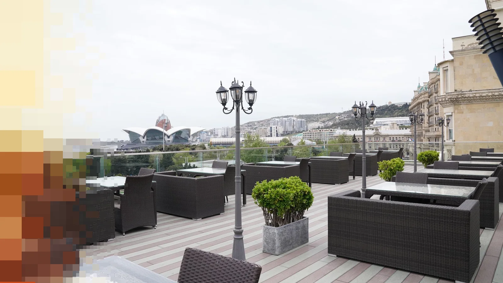 Terrasse på et tak med mørke loungemøbler, lyktestolper og utsikt over byen