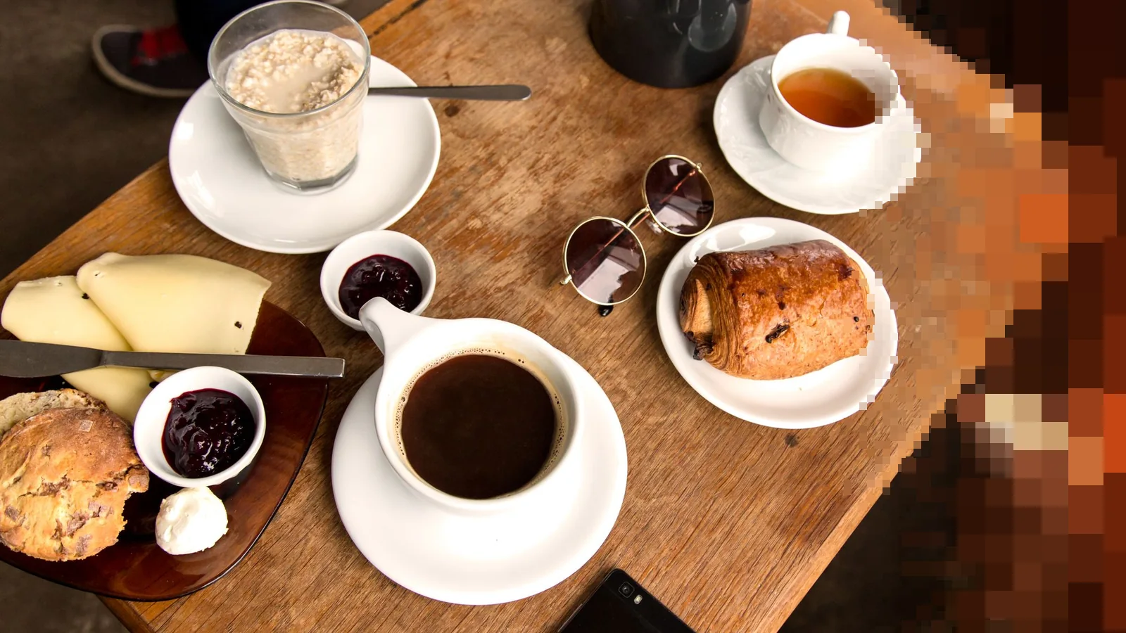 Et trebord sett ovenfra med kaffe, te, et bakverk, ost og syltetøy