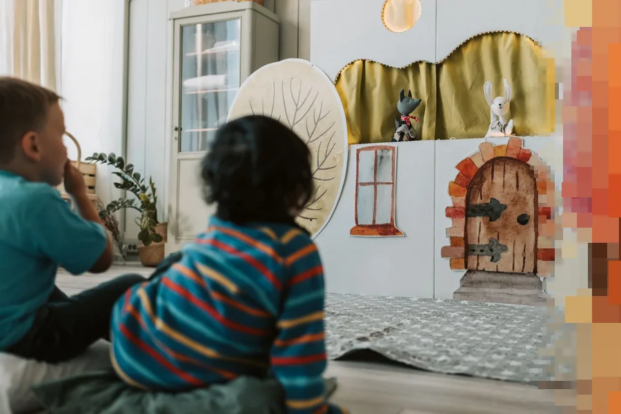 To barn som sitter på gulvet og ser på et dukketeater