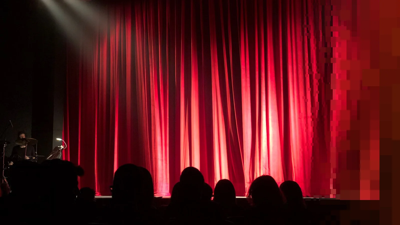 En teatersal med rødt teppe og publikum i silhuett foran scenen