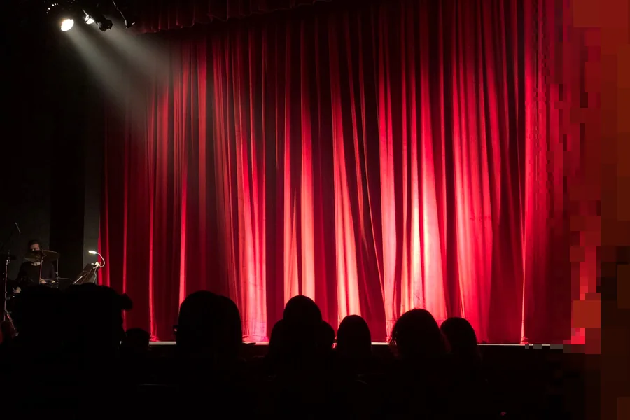 En teatersal med rødt teppe og publikum i silhuett foran scenen